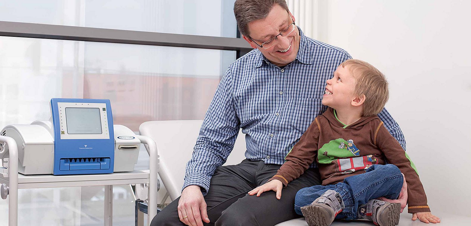 Vater mit Sohn auf Krankenbett sitzend